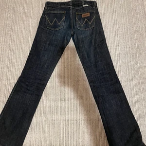Lågmidjade Wrangler jeans - Mörkblåa bootcut/straight low waisted jeans från Wrangler. Är tyvvär lite tajta på mig. W26, L32. Midja: 74cm innerben: 78cm