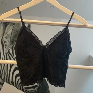 Spets-top - Svart topp i spets med justerbara axelband och resor i ryggen. I fint skick, passar perfekt som den är eller under kavaj och kan både kläs upp och kläs ner. Har ingen vaddering i kuporna men material ”bakom” spetsen så man kan absolut använda den utan BH. Storleken är XS och är true-to-size.