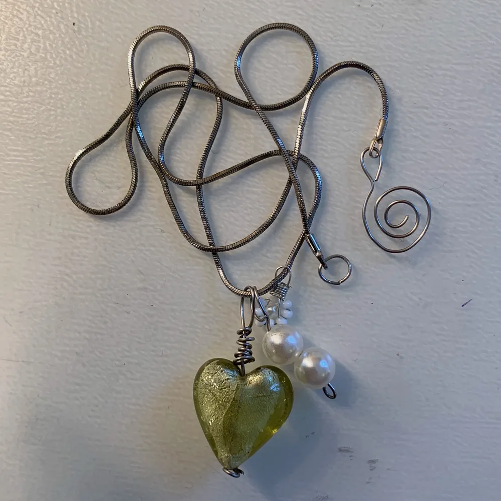 Silverkedja med ett grönt glashjärta, en liten vit blomma och två vita pärlor💚✨. Accessoarer.