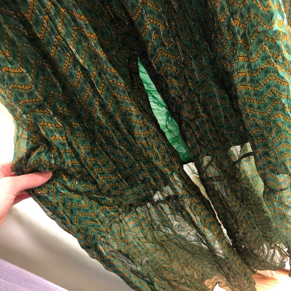 En lång vacker strandklänning i grön med finglirrigt mönster. V-ringad, flowig och lång slitt vid benet. Använd 1 gång. Är 178 cm lång och den släpar i backen.. Klänningar.