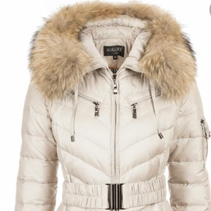 HOLLIES jacka pris kan diskuteras  - HOLLIES jacka Figursydd dunjacka från Hollies Stockholm fylld med 80% dun och 20% fjäder. På framsidan utav jackan finns det två stycken stolpfickor samt två bröstfickor som man inte kan öppna. På vänster arm finns det en ficka. Pälskanten på luvan som är sydd i tvättbjön  är avtagbar. Muddar finns sydda i armsluten.  Bältet kan man ta av om man vill utan att det påverkar jackans snygga passform. Jagckan finns i två olika färger, Svart och Beige/Creme.