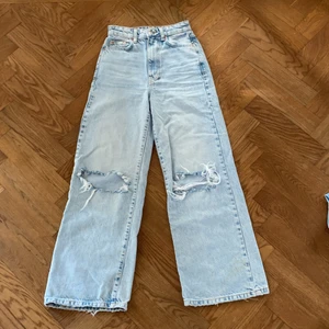 Jeans - Blåa jeans med slitningar från Gina tricot i storlek 30. Vida i benen men hål på knäna. Knapp och dragkedja upptill! Använda några gånger men i fint skick!
