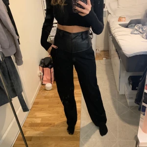 Kostymbyxor från NA-KD - Svarta kostymbyxor med läder detalj vid midjan. Jätteskönt material och bra längd på mig som är 169 cm. Använd ca 1-2 gånger.