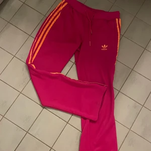 Adidasbyxor - Rosa utsvängda adidasbyxor med orangeräder, passar nån som är 160-165