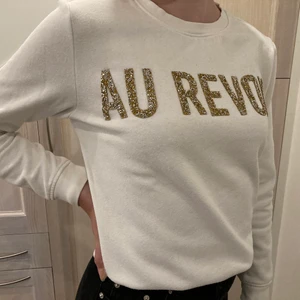 Sweatshirt med glitter tryck - Vit sweatshirt med glitter tryck. Perfekt till hösten och vintern. Lätt att matcha och styla. Trycket i glitter säger ”AU REVOIR”. Knapp använd, men är lite kort i ärmarna på mig.