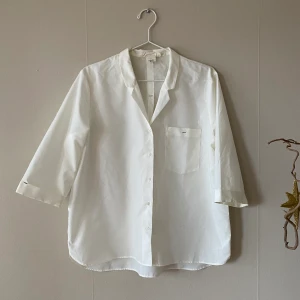 Grädd vit kortärmad skjorta  i strl 42  - En grädd vit kortärmad skjorta i storlek 42, den är V ringad och öppen i halsen med svarta små detaljer. Tröjan är ganska transparant 