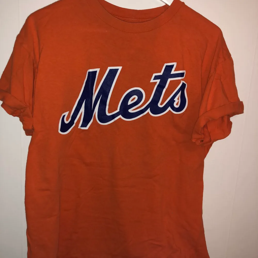 Orange T-Shirt med blått Mets tryck över bröstet. Uppvikta ärmar, den perfekta orangea färgen🧡🔥. T-shirts.