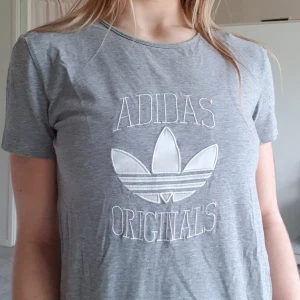 Grå Adidas T-shirt med broderat märke - Grå T-shirt från Adidas i storlek 34 (XS) men den passar definivt 34-38 (minst) eftersom den är väldigt stretchig. Jag på bilden har vanligtvis S för referens. Frakt tillkommer men kolla gärna på mina andra annonser för samfrakt!💞😋