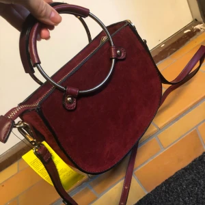 Snygg NY väska - Oanvänd vinröd väska i mockaimitation med lapp kvar. Snygga handtag med gulddetaljer. Kan användas både som axelremsväska eller handväska. 