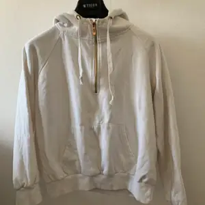 En vit hoodie med en fin detalj som är en Guld/bronset halvdragkedja samt en stor ficka