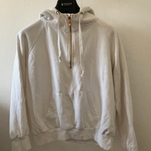 Hoodie - En vit hoodie med en fin detalj som är en Guld/bronset halvdragkedja samt en stor ficka