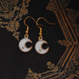 Örhängen med vita månar - Handgjorda örhängen med guldpläterad berlock och nickelfria krokar 🌙 På min profil finns fler örhängen med berlocker i flera andra storlekar, färger och former! 🪐 Köp 1 par för 40kr, 2 par för 70kr, 3 par för 100kr! Örhängena levereras i en fin liten presentpåse. Frakt på 13kr tillkommer 💫