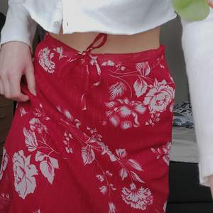 En röd blommig kjol med volanger där nere. Trendig med early 2000's vibe. Är mid length och passar nog XS- M genom att man kan snöra åt den i midjan