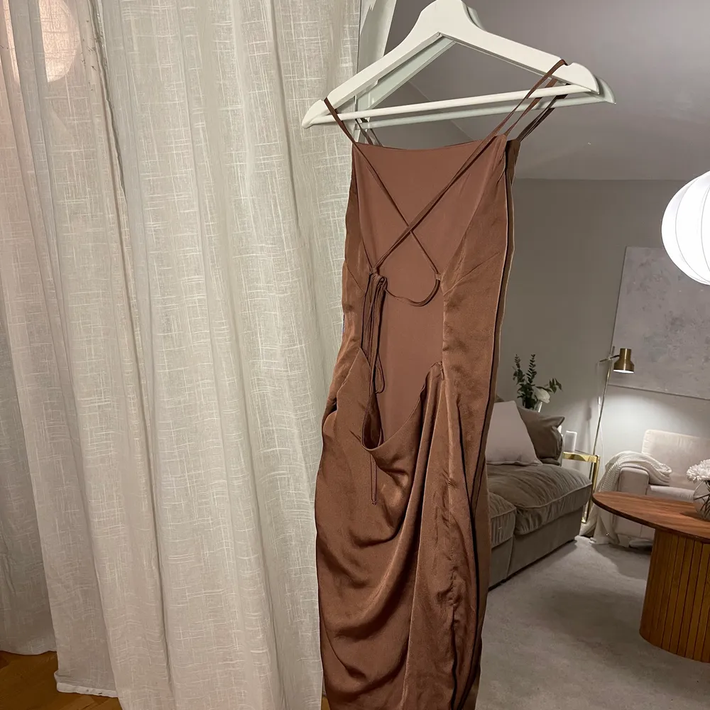 Super fin bronze klänning, från NELLY. Storlek 36. Lite längre på ena sidan med lite ”skrynkligt”  och kortare på andra. Öppen rygg. Går att reglera banden själv. . Klänningar.