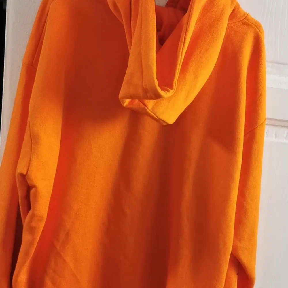 Här har vi en orange hoodie med ett tryck där det står 