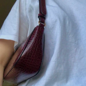 Vinröd baguettväska med gulddetaljer  - Nästan oanvänd vinröd baguetteväska från Lindex. I mycket gott skick. Inköpt i höstas men säljer pga att jag inte använder den. Nypris: 250 kronor. Endast leverans, köparen står för frakt!