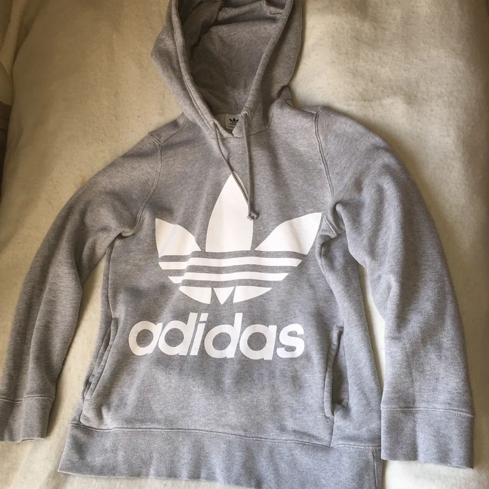 Ljusgrå Adidas huvtröja med tre-foil logo fram och stor genomgående ficka. Använd men i fint skick. Storlek 34-36, rymlig. UK 8. Hoodies.