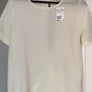 Ny topp med detaljer i ryggen - Fin vit topp - aldrig använd. Nypris 299kr. Fin detalj i ryggen där den är öppen. 