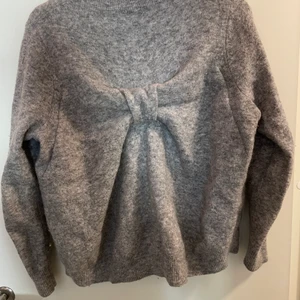 Stickad tröja med rosett bak - Fin stickad tröja från Cos. Stor rosett på ryggen.