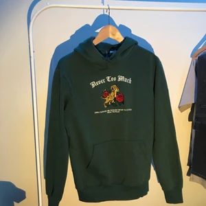 Hoodie - Grön hoodie med broderat tryck i storlek small. Trycket är på framsidan. Snörena är knutna men går såklart att ta loss.