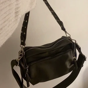 En militärgrön väska från ULRIKA DESIGN - Väskan köptes för ca 2 år sen men användes bara under sommaren 2019 och inget efter det. Den är i bra skick och har 4 synliga fickor utanpå och 2 mindre fickor inuti. Väskan har även 2 band, ett kortare och ett längre perfekt över axeln. Den används aldrig mer och vill därför bli av med den. Utanpå syns ett militärgrönt skinn och inuti ett svartvitt leopardprint. Köpt för 599kr. 