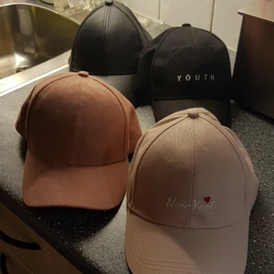 Kepsar - 4 olika kepsar. Längst upp till höger: svart läder keps. Längst upp till vänster: Youth keps i tyg. Längst ner till höger: laxfärgad sammet tyg. Längst ner till vänster: ljus rosa keps i tyg. 50kr/st eller 150kr för alla