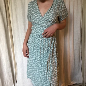 Grönblå omlottklänning med vitt blommönster - Supersöt skjusterbar omlottklänning perfekt till sommaren i en ljus grönblå nyans och med ett vitt blommönster!🕊 Köpt på secondhand men aldrig använd så superfint skick! Från Noa Noa ursprungligen så jättefin kvalitet. Storleken är M men passar på S också då den är skjusterbar! Köparen står för frakten!🤍