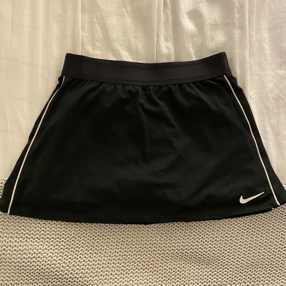 Tenniskjol från Nike. Rak modell, svart med vita streck på sidan. Svarta undershorts.. Kjolar.