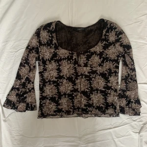 Blus  - Svart blus med blommor och flare i ärmarna och knytningsdetalj fram