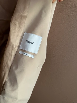 Filippa K kavaj  - Beige kavaj från Filippa K. Den har varit trasig så den är ihopsydd inuti på ett antal ställen, därav det låga priset. 