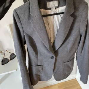 Grå kavaj - Säljer denna kavaj då den är för liten. Den är i strl 38 men skulle säga att det är liten i storleken❤️ köparen står för frakten 