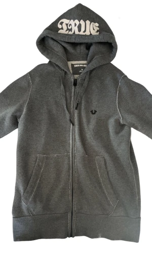 True Religion Hoodie - Säljer tröjan för att den ej kommer till användning längre. Tröjan har extremt bra kvalite och väldigt tung bomull som isolerar väldigt bra, och zip:en funkar utmärkt. Den är större i passformen och passar S/M   Köptes för 165€ 2019