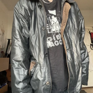 Snygg thriftad jacka - Snygg thriftad vinterjacka i fakeläder med manchester krage och linning, ca storlek L, saknar knapp vid fickan och har några små hål samt ett stort som är visat på bild. Ändå väldigt snygg och varm för v vintern