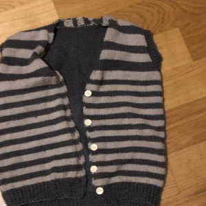 Stickad randig väst  - Kort stickad grå/brun och beige randig väst. Fint skick. Längd: 51cm Ärm-omkrets: 31cm