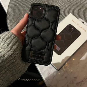 Skal iPhone 13 - Säljer mitt supersnygga helt nya skal från Ideal of sweden då jag köpt fel modell. Skalet heter Puffy Black och är perfekt nu i vinter då man kan trä in fingrarna bakom tyget.  Nypris 499kr. Säljer för 150kr.❤️