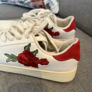 Sneakers - Sneakers med röda detaljer och rosor på sidan. Är storlek 40 men dom är som storlek 39. Köparen står för frakt💕