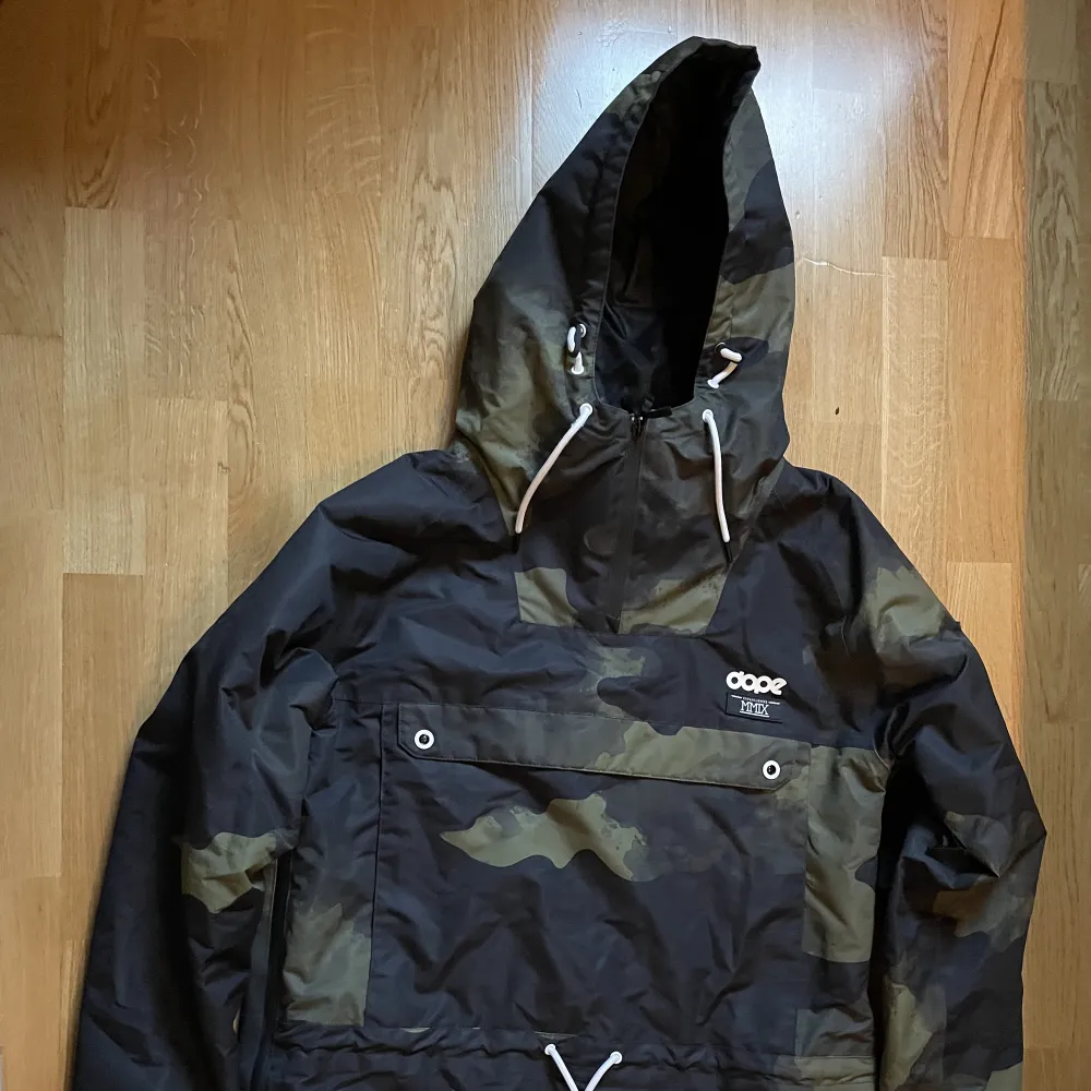 Anorak skidjacka från märke Dope. Militärmönster. Två st fickor på magen. En ficka för liftkort på ena ärmen. Dragkedjor på sidorna för ventilation. Luva som går att få över skidhjälm. Använd 1 vecka i fjällen. Inget tecken på slitage. . Takit.