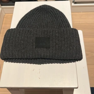 Acne Pansy Face Hat (mörkgrå) - Acne mössa i mörkgrå färg. Välbevarad och i fint skick!  Hämtas på Kungsholmen.