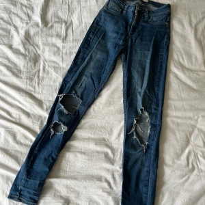 Blåa jeans - Ett par blåa slim jeans med slitningar från Ginatricot i storlek M.