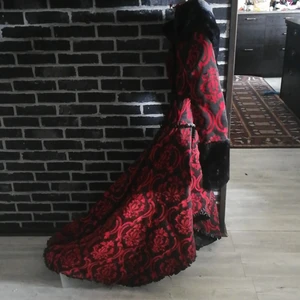 Svart röd kapa  -  svart kapa med röt mönster svarta knappar framtill sör knäpnig  snörning baktill i ryggen fuskpäls i krage o armarna lång bak till kortare fram till sparsamt använd är lite sliten längst ner på spetsen på ett stele anars som ny Katt o Hund fins i hemmet    dena prudukt kostar 156€ som ny  