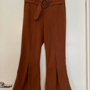 Byxor med tillhörande skärp strl S - Ett par byxor med retro-feeling i en fin mörkrödbrun färg. Lite croppade, passar för mig som är 160 cm. Dragkedja bak och skärp med trädetalj. Ganska stretchiga.