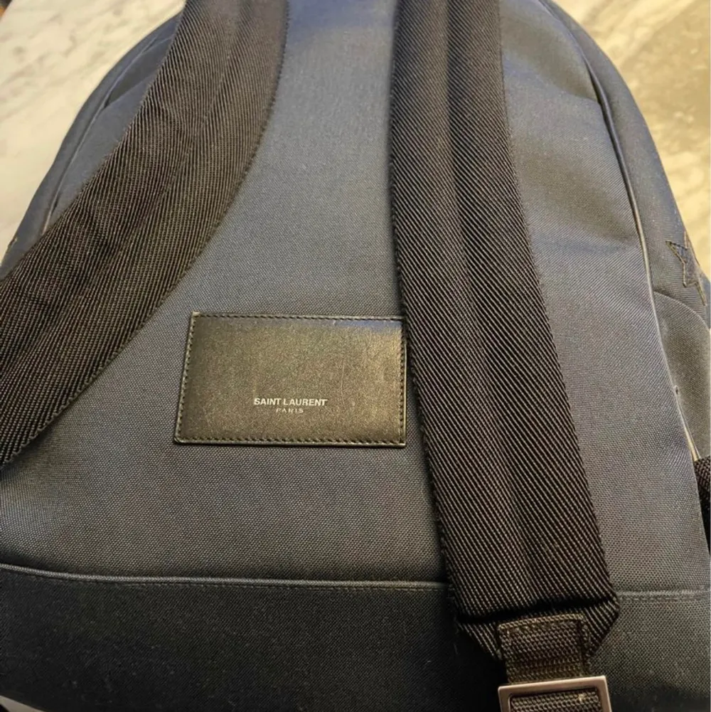 ryggsäck från saint Laurent i mörkblått med star motivet.  Bra väska som rymmer det mesta, laptop/iPad fack, nyckelhållare. Nypris 8995 Knappt använd, endast väskan säljs. Väskor.
