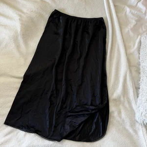 Vintage svart slipkjol i satin - Vintage svart slipkjol från Beyond Retro i fint skick. Passar en xs-m och har stretchig midja. 