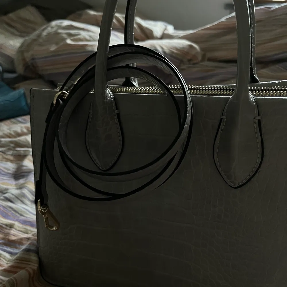 En grå stilren väska som jag köpte för ett tag sen men aldrig använde. Går att använde som både handväska och axelväska! . Väskor.