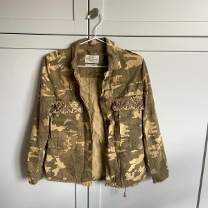 Grön Jacka Bershka - Säljer en grön jacka i storlek xs/s. Det går att knyta åt den i midjan så att den blir mer figursydd. Sparsamt använd! Kontakta mig vid intresse. Fraktkostnad ingår inte i priset