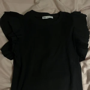 Volangtopp från Zara - Superfin svart volangtopp från zara i iprincip nyskick, använd fåtal gånger. Storlek S och sitter bra på mig som är 168 cm lång. Säljer pga den inte kommer till användning.