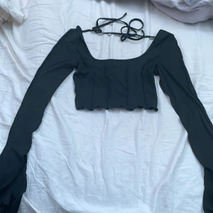 Svart croptop - Svart croptop från SHEIN. Långa ärmar med slitt längst ut. Den har knytning vid skulderbladen. Aldrig använd och säljs för att den är för liten. Storlek xs. Original pris 100kr