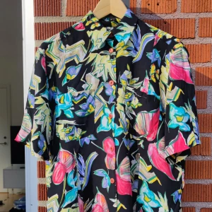 Mönstrad skjorta blus - Mörkt och blommigt grafiskt mönster.  Den går att knyta på olika sätt runt midjan med flärparna i tyget, se sista bilden. 