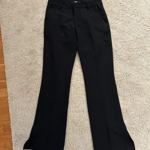 Lågmidjade kostymbyxor - Lågmidjade utsvängda  svarta kostymbyxor från Bikbok med slits där nere. De PERFEKTA kostymbyxorna!! Har blivit för små😢 