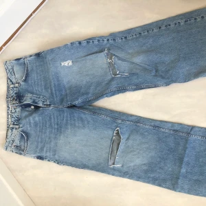 Jeans BikBok - Ett par blå vida jeans med hål på knäna och andra slitningar. Fransiga längs bristen. Från BikBok i storlek 40. Frakt tillkommer📦